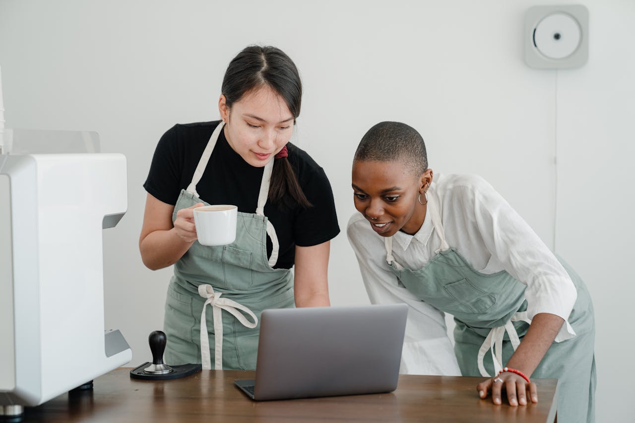 Young Asian coffee house worker explaining to new African American coworker how to use special computer program during break at work